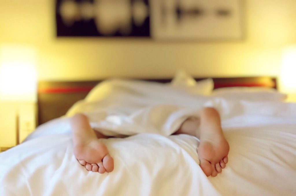 Two feet sticking out of bed. Woman laying face down in bed, all that is visible is her feet sticking out of the white sheets.