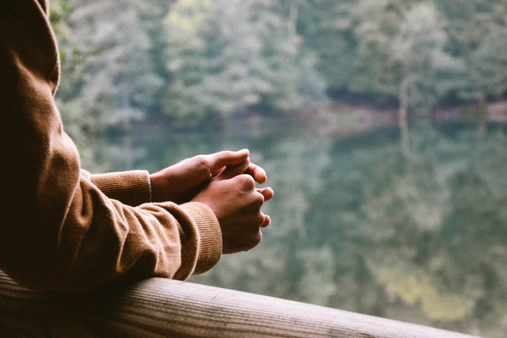 Man's hands crossed overlooking a lake surrounded by trees.