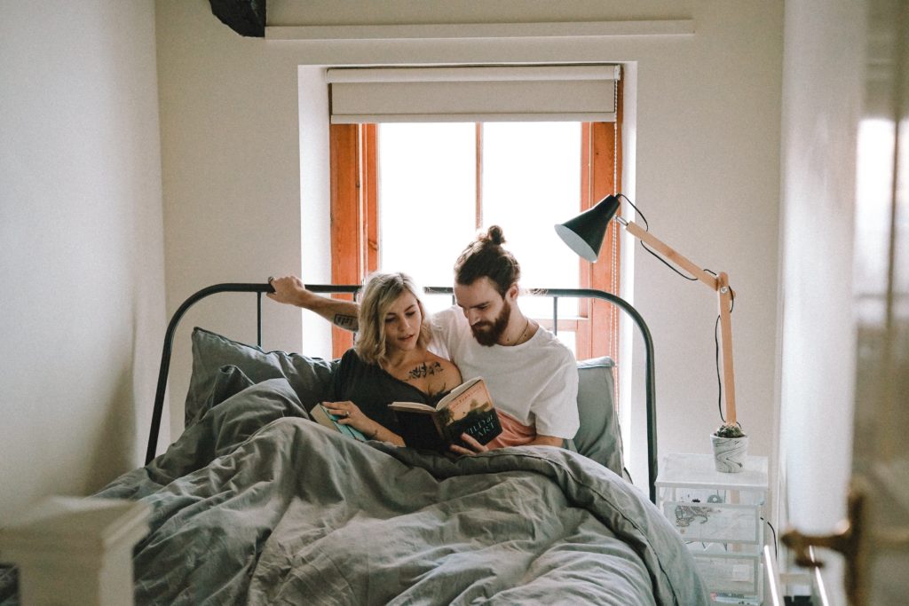 Man and woman laying in bed together talking about anxiety and reading a book.